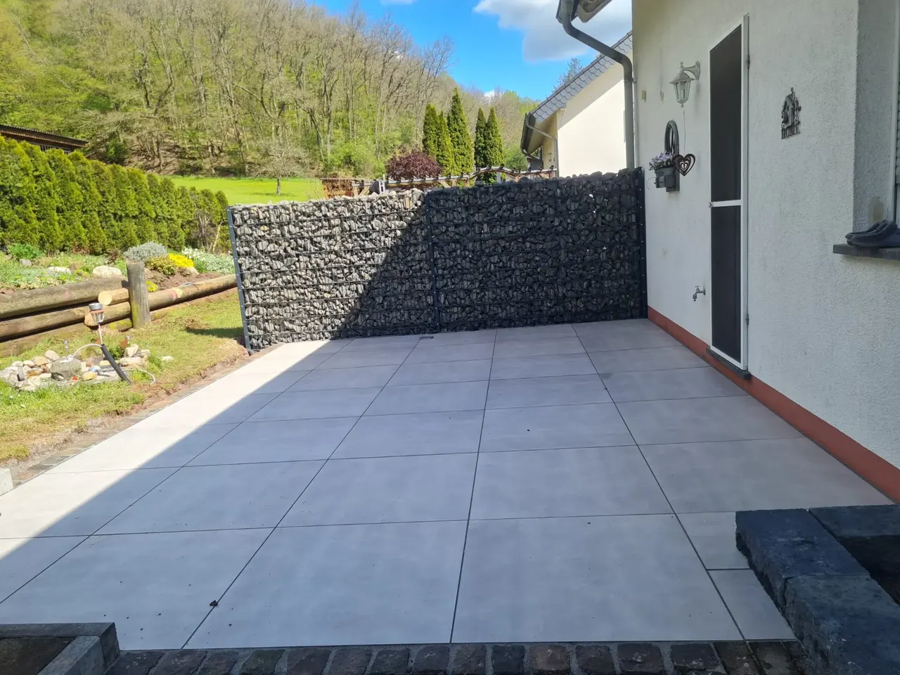 Terrasse mit hellgrauen Platten und Gabionen-Sichtschutzwand