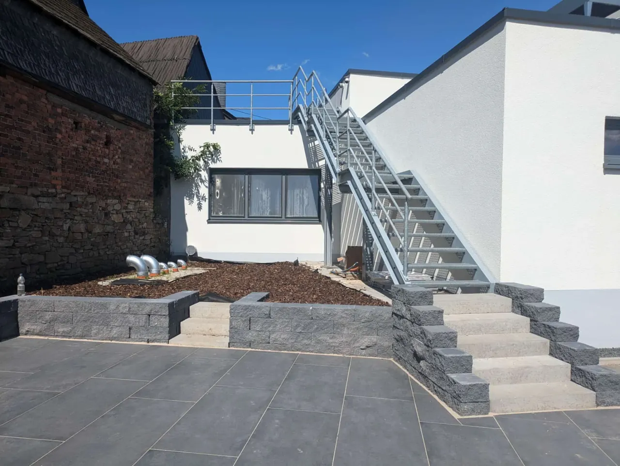 Terrasse mit anthrazitfarbenen Platten, Mauerscheiben und Blockstufenanlage