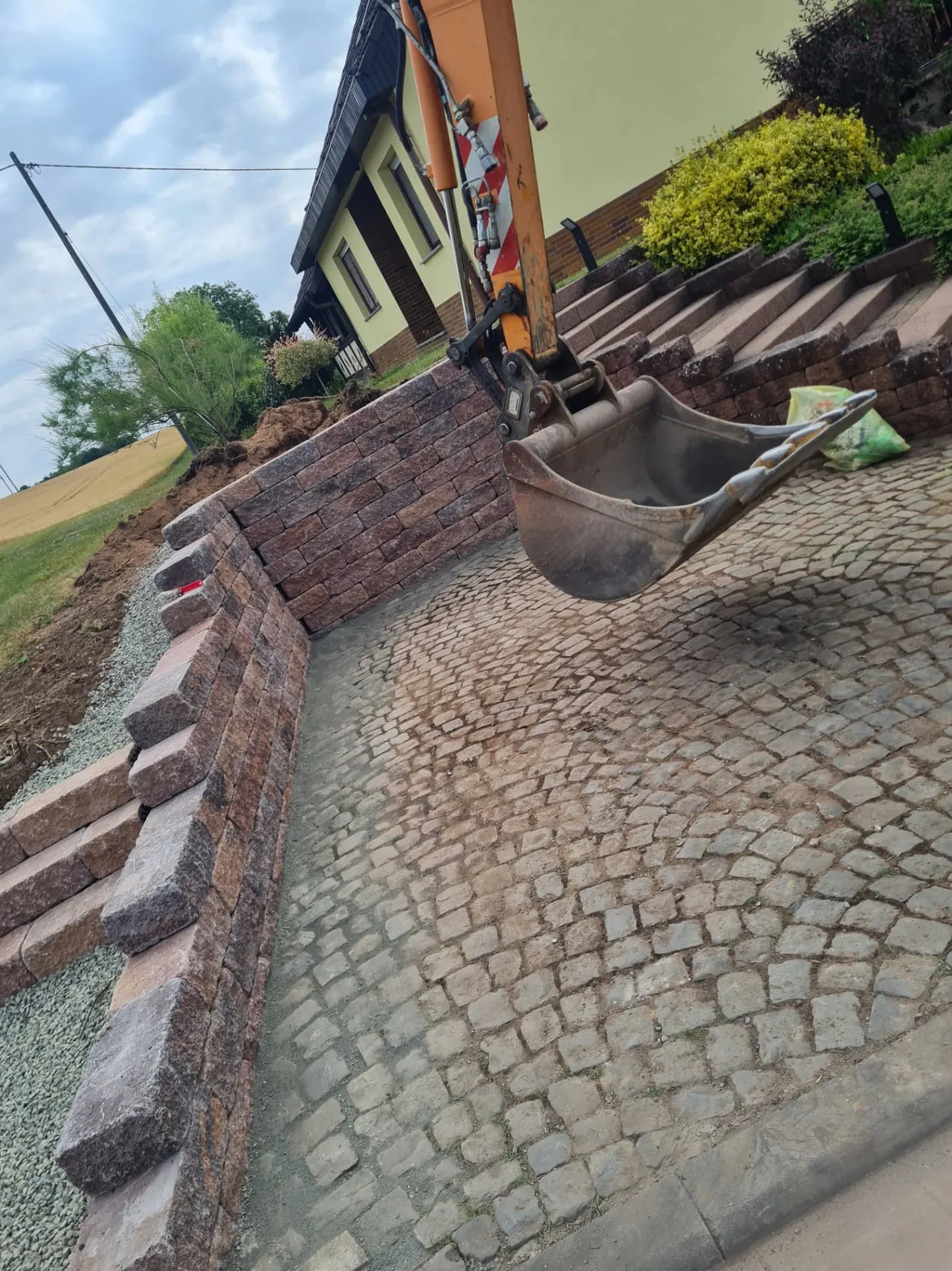 Natursteinmauer mit Treppenanlage, Pflasterfläche und bepflanztem Hang